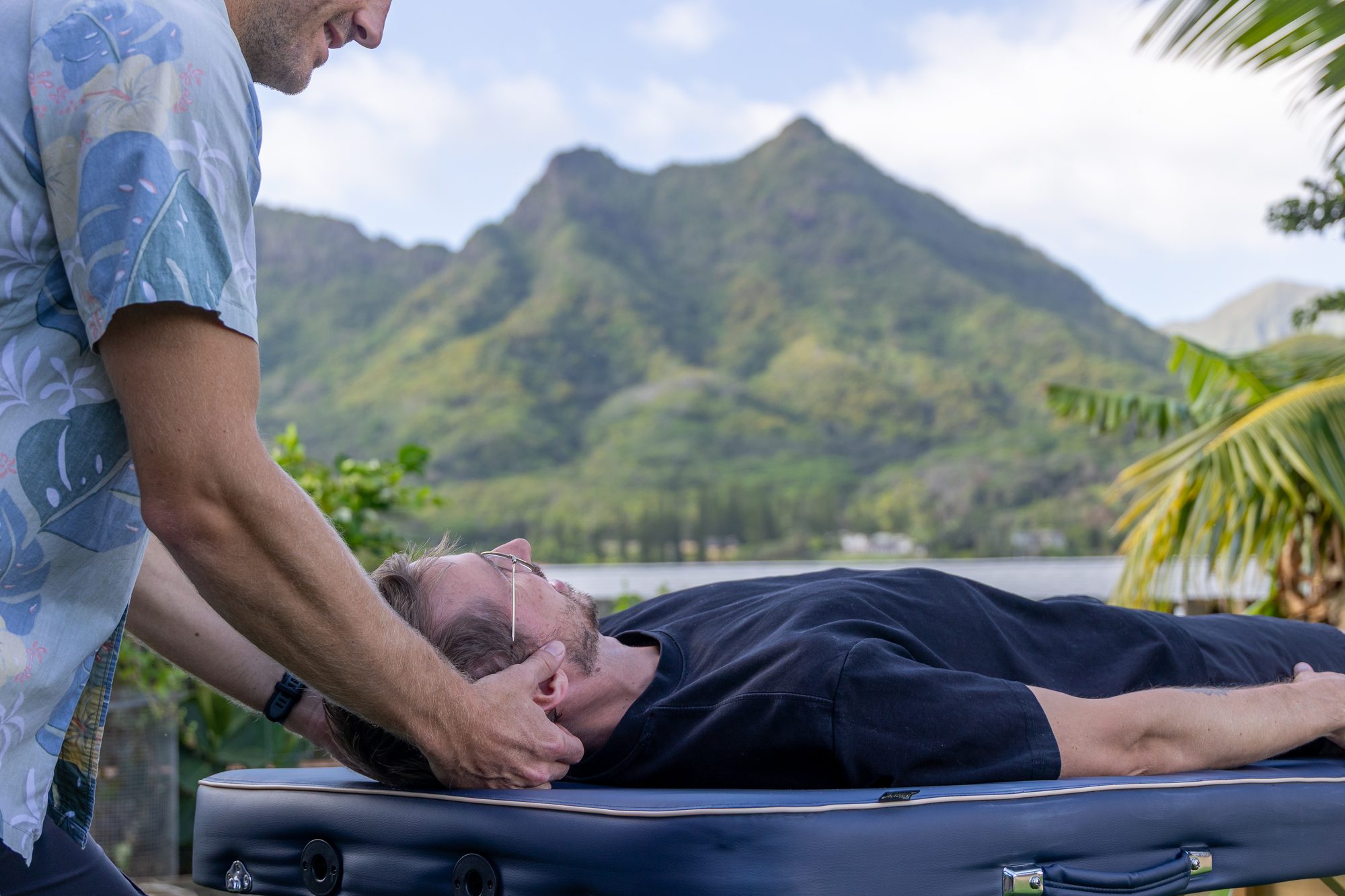 Evan Lewis performing a hands-on cervical assessment with the Olomana ridge in the background